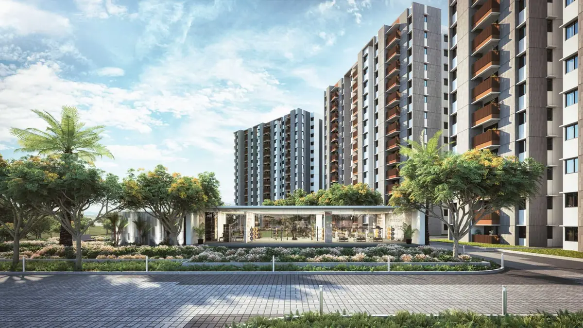 The clubhouse at Mahindra World City, a low glazed building set among mature flowering trees, with residential towers behind it.